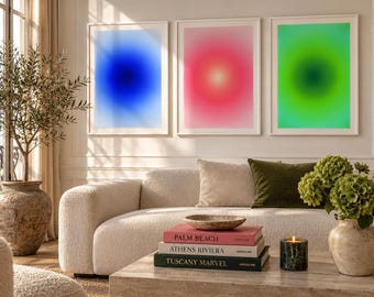 May include: Three framed rectangular wall art prints featuring gradient aura designs in vibrant blue, pink, and green. The prints are displayed in white frames above a cream-colored sofa, with a stack of books titled Palm Beach, Athens Riviera, and Tuscany Marvel.