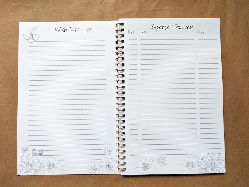 Pode incluir: Um caderno branco de espiral com uma se&ccedil;&atilde;o de lista de desejos e um rastreador de despesas. O caderno tem um design de borboleta e flores.