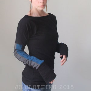 Puede incluir: Una camisa negra de manga larga con cuello de barco y detalles azules y grises en las mangas. La camisa es entallada y tiene una longitud ligeramente más larga en la espalda.