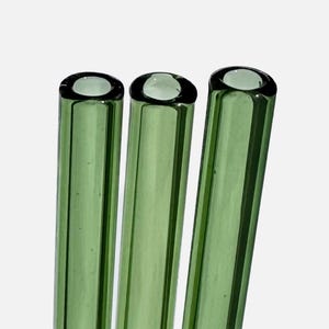 Three green glass straws are arranged in a row against a white background.