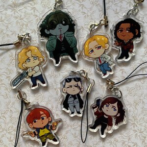 May include: A collection of seven clear acrylic charms featuring chibi-style illustrated characters. Each charm includes a black cord strap with a silver-tone metal clasp. The characters display various outfits, hair colors, and poses, some holding small weapons.