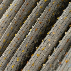 Pode incluir: Close-up de um tecido cinza texturizado com listras pretas verticais e manchas amarelas, laranja e azuis espalhadas. O tecido parece estar dobrado ou plissado, criando um padrão diagonal.