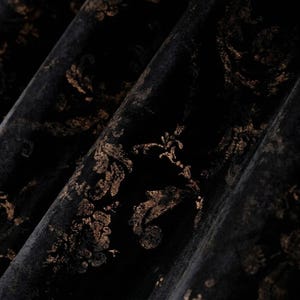 May include: Close-up of black fabric with a gold floral pattern. The fabric is folded, revealing its texture and design. The gold pattern has a vintage, ornate style, creating a luxurious appearance.