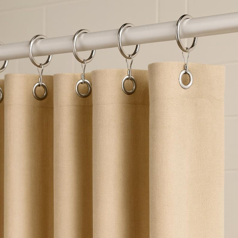 Puede incluir: Cortinas de tela beige colgadas de una barra blanca con anillos met&aacute;licos plateados. Las cortinas est&aacute;n hechas de un material texturizado y est&aacute;n parcialmente cerradas, creando pliegues suaves. La paleta de colores neutros sugiere un dise&ntilde;o simple y elegante.