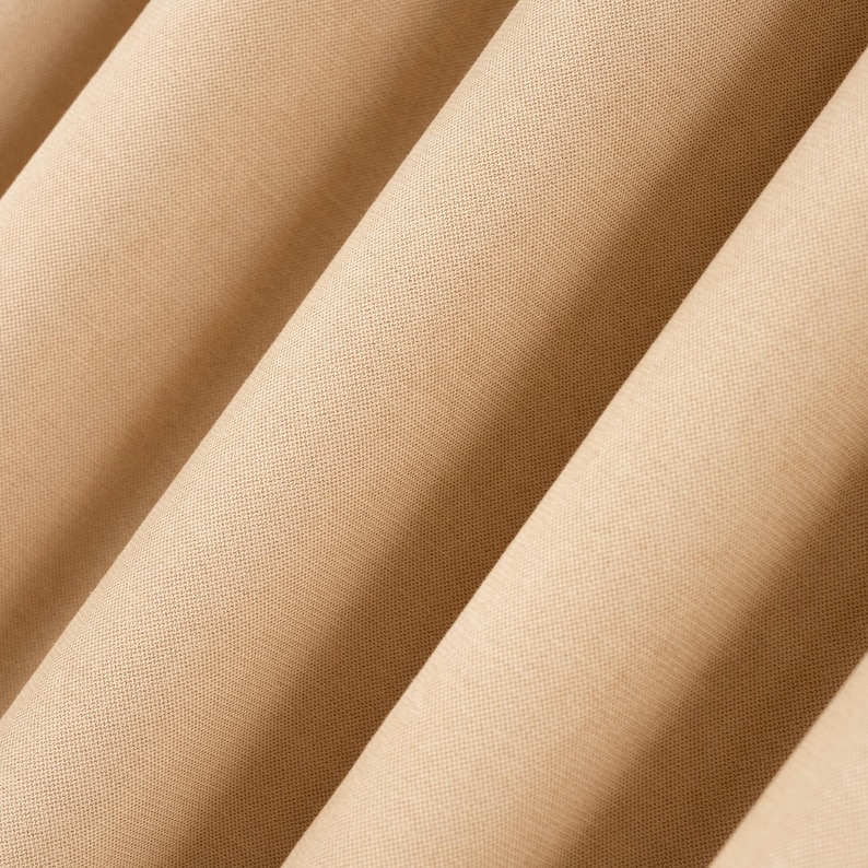 Puede incluir: Primer plano de tela beige doblada. La tela tiene una textura sutil y est&aacute; dispuesta en pliegues diagonales, creando una sensaci&oacute;n de profundidad. El color es un tono c&aacute;lido y neutro, adecuado para diversas aplicaciones.