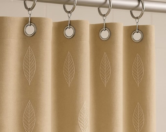 Puede incluir: Cortina de ducha beige con diseño de hojas bordadas. La cortina cuelga de una barra plateada con anillos metálicos. El diseño de hojas se repite en los paneles, creando una estética natural y coordinada.