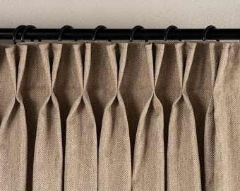 May include: Close-up of beige linen curtains with a pleated design, hanging from a black metal rod with black rings. The curtains have a textured appearance and are partially closed, creating soft folds.