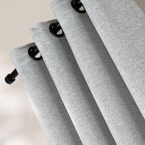 Puede incluir: Primer plano de cortinas grises claras con estampado de espiga y ojales negros. La tela está doblada en líneas diagonales suaves, creando un efecto texturizado. Las cortinas cuelgan de una barra negra.