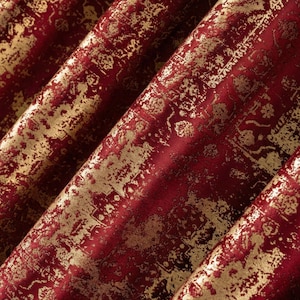 Può includere: Primo piano di un tessuto lussuoso con sfondo rosso intenso e motivo dorato invecchiato. Il tessuto è piegato, mostrando la consistenza e la lucentezza del materiale. Il design ha un aspetto antico e ornato.