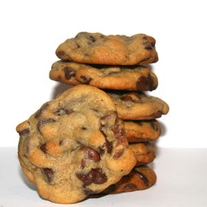 May include: A stack of six chocolate chip cookies, with the bottom cookie partially obscured by the others. The cookies are golden brown and have a slightly crispy texture.