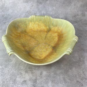 May include: A ceramic bowl featuring a tri-lobed rim with ribbed detailing at each of the three points. The interior displays a blended gradient of pale yellow and soft green tones, creating a mottled, textured appearance across the surface.