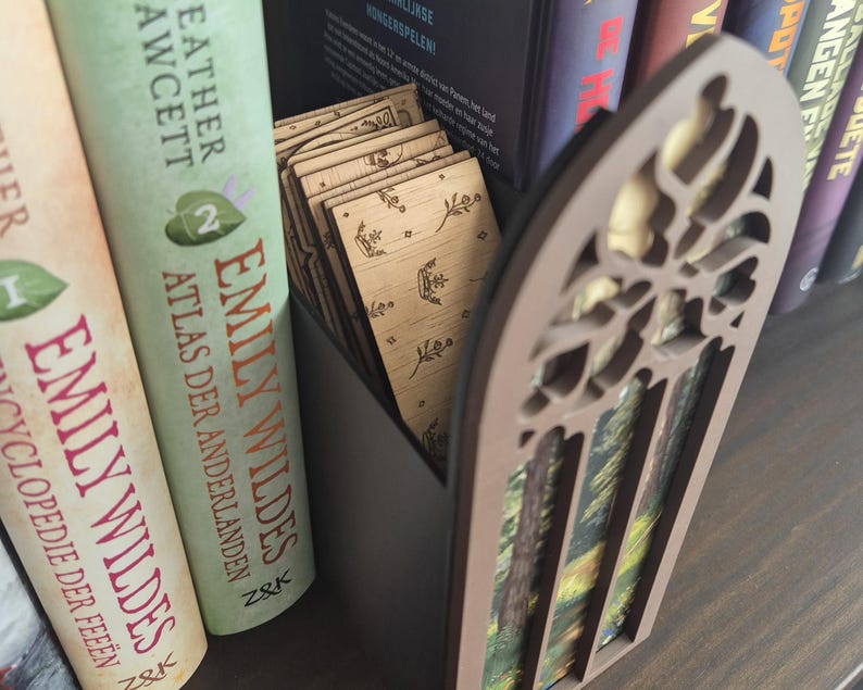 May include: A dark grey rectangular container holding several light-coloured wooden rectangular cards, each featuring a small engraved floral design. The container has a brown, arched, laser-cut decorative front panel with a forest scene print.