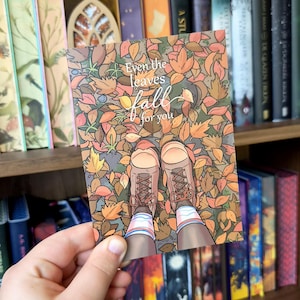 Op de afbeelding: Een rechthoekige kunstdruk met een bovenaanzicht van bruine veterschoenen en gestreepte sokken in een hoop kleurrijke herfstbladeren. De tekst Even the leaves fall for you staat in witte letters in het midden van de afbeelding.
