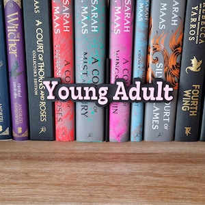 Op de afbeelding: Een boekenkast met een selectie boeken, waaronder "A Court of Thorns and Roses" van Sarah J. Maas, "The Witcher" van Andrzej Sapkowski en "Iron Flame" van Rebecca Yarros. Een roze en zwart bord met de tekst "Young Adult" is voor de boeken geplaatst.