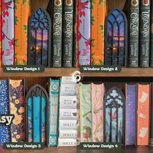 May include: Four black gothic-style window book inserts displayed on a shelf between various hardback books. Each insert features a detailed frame with a unique printed scene inside, including a campfire at sunset, a forest, and a red dragon.