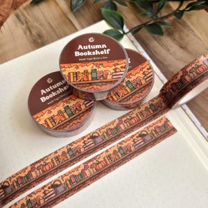 Op de afbeelding: Drie rollen decoratieve washi-tape met het label Autumn Bookshelf, Washi Tape 15mm x 10m. De tape bevat een herhalende illustratie van een boekenplank met boeken, pompoenen, paddenstoelen en eekhoorns in oranje, bruine en groene tinten.