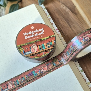 Op de afbeelding: Een rol washi tape met een grillig "Hedgehog Bookshelf" ontwerp. De tape heeft een herhalend patroon van egels, boeken en bladeren. De tape is 15 mm x 10 m.