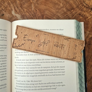 Könnte beinhalten: Ein Holz-Lesezeichen mit einem Ticket-Design. Das Lesezeichen ist mit den Worten "Escape Reality" und "One Chapter at a Time" graviert.