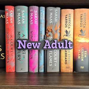 Op de afbeelding: Een boekenkast met een selectie fantasy romans, waaronder titels van Sarah J. Maas en Rebecca Yarros. Een paars-zwart bord met de tekst "New Adult" is tussen de boeken geplaatst.