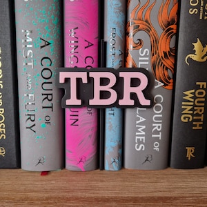 May include: A close-up of a bookshelf with a pink and black "TBR" book marker. The bookshelf is filled with fantasy novels with titles like "A Court of Thorns and Roses" and "A Court of Mist and Fury".