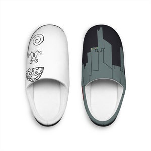 Pode incluir: Um par de chinelos brancos. Um chinelo apresenta um design abstrato em preto e branco, enquanto o outro exibe uma paisagem urbana cinza sobre um fundo preto. Os chinelos têm um interior macio e acolchoado.