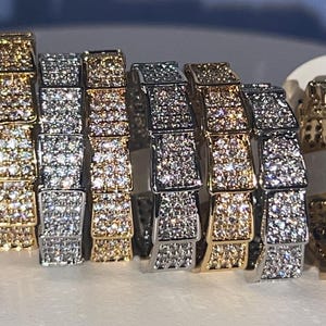 May include: A set of eight hoop earrings with a square-shaped design. The earrings are made of silver and gold metal and are encrusted with small, clear stones.