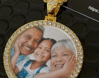 May include: Gold chain necklace with a round pendant featuring a photo of three people surrounded by clear cubic zirconia stones.