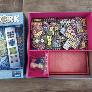 Peut inclure: Bo&icirc;te de jeu de soci&eacute;t&eacute; ouverte, intitul&eacute;e "Patchwork Nordic". La bo&icirc;te bleue clair contient des pi&egrave;ces de jeu &agrave; motifs, des boutons, un plateau de jeu et de petits &eacute;l&eacute;ments. Les pi&egrave;ces de jeu sont mesur&eacute;es en centim&egrave;tres.