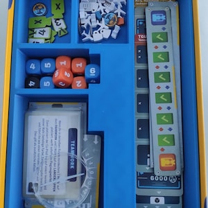 Può includere: Un tabellone di gioco blu con vari pezzi di gioco, tra cui dadi, carte e gettoni. Il tabellone ha scomparti per riporre i pezzi di gioco. Il testo sulle carte include "TEAMWORK" e "ATL Hartsfield-Jackson".