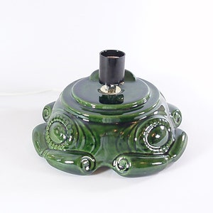 May include: A vintage green ceramic Christmas tree base with a glossy finish. The base has a round top with a black light socket and a decorative, textured design. The base is approximately 8 inches in diameter.