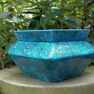 May include: A turquoise blue planter with a geometric shape and a speckled finish. The planter has a gold fleck design and is made of ceramic.