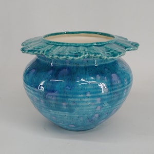 May include: A turquoise ceramic planter with a scalloped rim and a blue and white glaze. The planter has a speckled and streaked design.