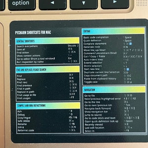 May include: A close-up of a sticker showing keyboard shortcuts for the PyCharm software on a Mac computer. The sticker is divided into sections for general shortcuts, find and replace, compile and run, editing, and navigation. Each section lists a shortcut key combination and its corresponding action.