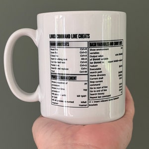 May include: White ceramic mug with a large handle, featuring a printed reference guide for Linux command line cheats. The text includes Nano shortcuts, Bash variables, and process management commands. A useful gift for programmers and tech enthusiasts.