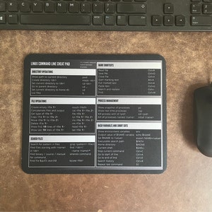 May include: A black and white cheat sheet for Linux command line commands. The cheat sheet is divided into sections for directory operations, file operations, process management, bash variables and short cuts, and name shortcuts. The cheat sheet is printed on a black mouse mat.