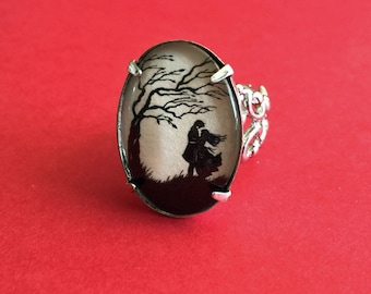 Op de afbeelding: Een zilveren ring met een ovale cameo met een silhouet van een stel dat onder een boom staat. De cameo is gezet in een zilveren ring met een delicaat ontwerp.