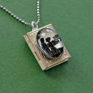 May include: A silver locket necklace with a cameo featuring a black and white silhouette of two people standing in front of a building.