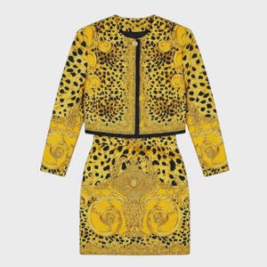 May include: A two-piece set consisting of a long-sleeved cropped jacket and a matching skirt. Both pieces feature a vibrant yellow and black leopard print pattern combined with intricate gold-toned baroque scrollwork and a central Medusa head motif.