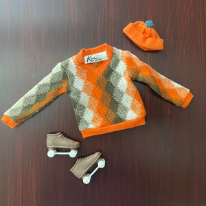 May include: Orange and green patterned sweater with a V-neck, a blue and orange beanie, and two brown roller skates.