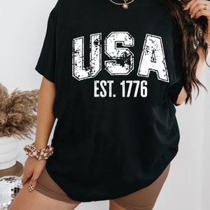 May include: Black t-shirt with a white distressed graphic that says "USA EST. 1776".