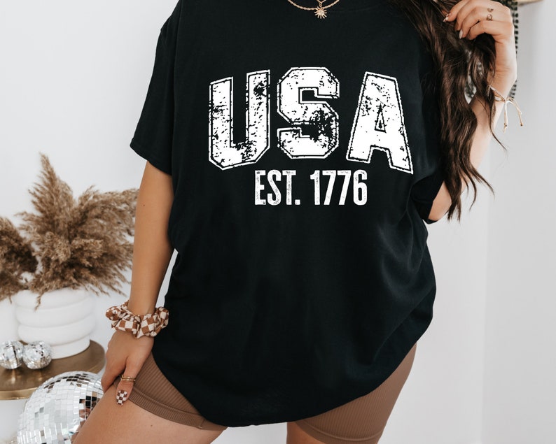 May include: Black t-shirt with a white distressed graphic that says "USA EST. 1776".