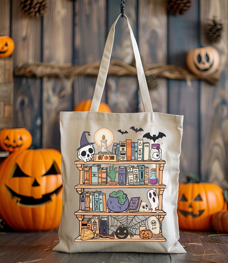 Puede incluir: Bolso tote de lona beige con un dise&ntilde;o de estanter&iacute;a de Halloween. La ilustraci&oacute;n incluye una calavera con sombrero de bruja, libros, un caldero, un fantasma y una telara&ntilde;a. El bolso tiene un asa de color claro y cuelga sobre un fondo de madera.