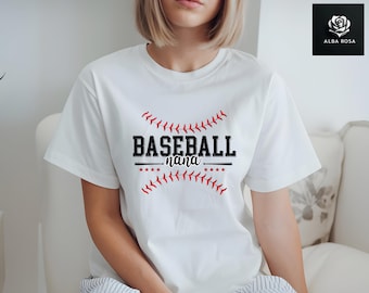 May include: A white short-sleeved t-shirt featuring a graphic design with the text BASEBALL nana in black, flanked by red baseball stitching patterns, small black stars, and a horizontal line resembling a baseball bat across the chest.