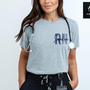 May include: A gray t-shirt with the text "RN Sophia" printed on the front. The shirt is being worn by a person with a stethoscope around their neck.