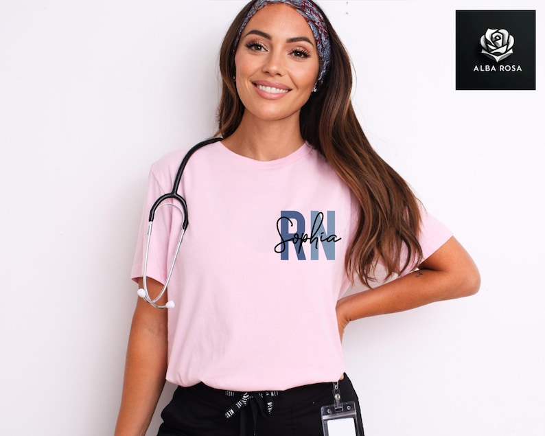 May include: A pink t-shirt with a blue and gray "RN" design and the name "Sophia" written in cursive. The shirt is being worn by a person with long brown hair and a headband.