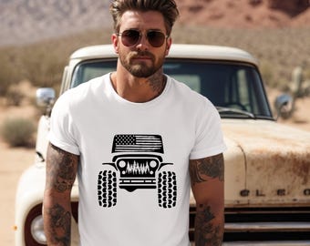 May include: A white short-sleeved t-shirt featuring a black graphic print on the chest. The graphic depicts the front view of an off-road vehicle with a stylized American flag on the roof and a forest silhouette integrated into the grille area.