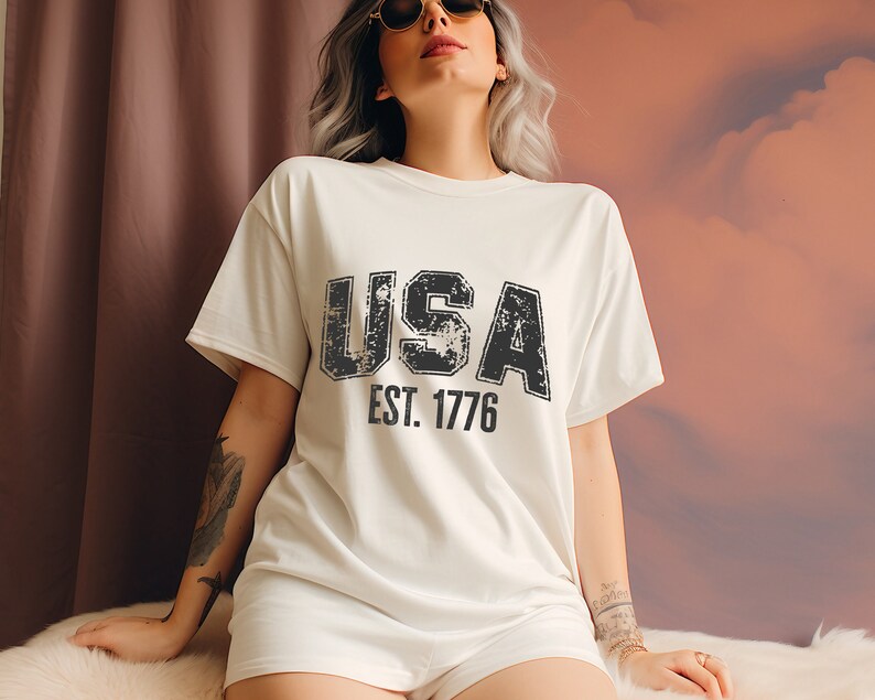 White t-shirt with a black distressed graphic that says 'USA EST. 1776'.