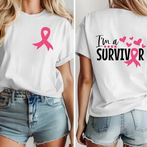 Op de afbeelding: Wit T-shirt met een roze lint aan de voorkant en de tekst "I'm a SURVIVOR" met een roze lint aan de achterkant.
