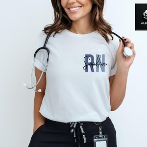 May include: White t-shirt with the text "RN Sophia" in blue and black lettering. A stethoscope is draped around the neck of the person wearing the shirt.