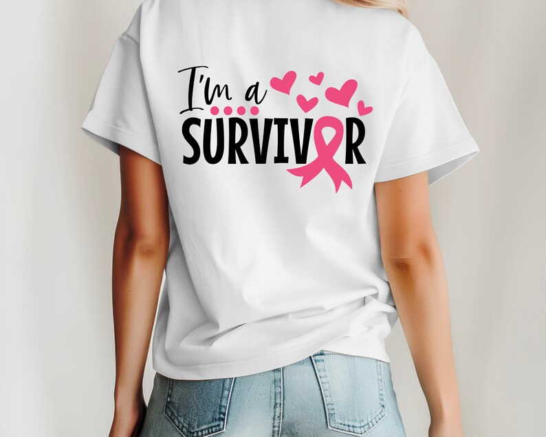 Op de afbeelding: Wit T-shirt met de tekst "I'm a SURVIVOR" in zwart met een roze lint en roze harten.